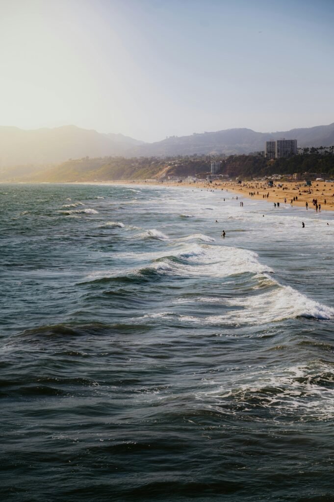 Vibrant waves crashing on a sunlit beach with distant mountains and buildings.